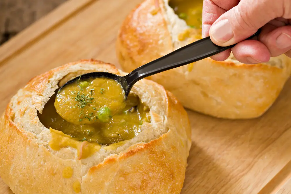 split pea soup in bread bowl with hand pulling spoonful out