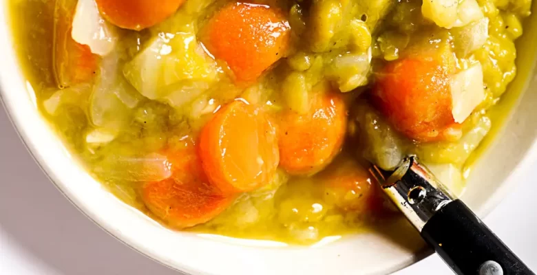 vegan split pea soup with carrots in white bowl and black handled spoon