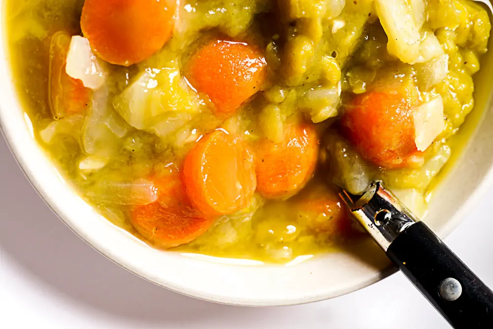 vegan split pea soup with carrots in white bowl and black handled spoon