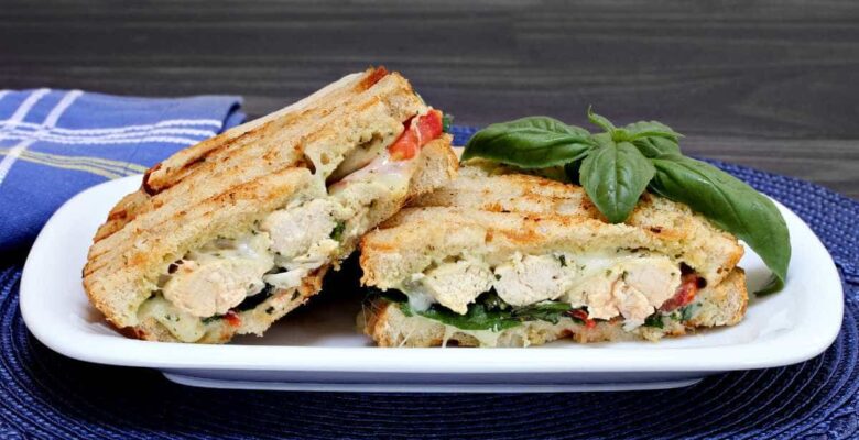 chicken caprese sandwiches with basil on a white platter