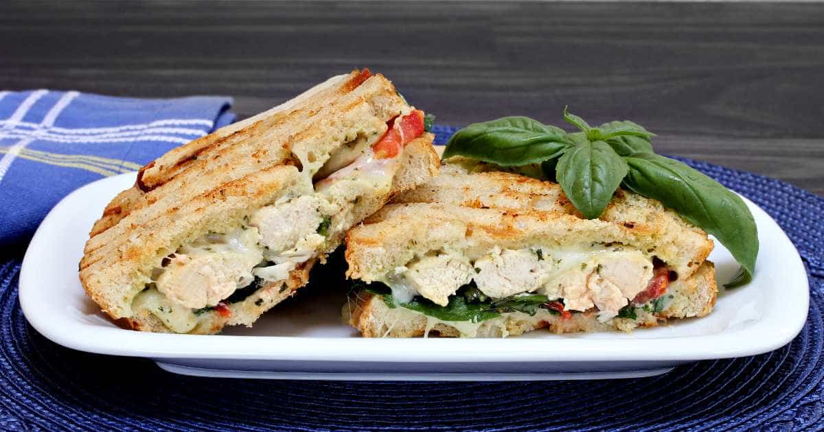 chicken caprese sandwiches with basil on a white platter