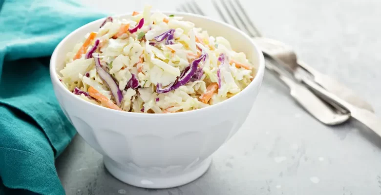 tri-color coleslaw in white bowl with green napkin and fork to the sides