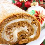 pumpkin roll with cream cheese on a white platter with holiday ornaments in background