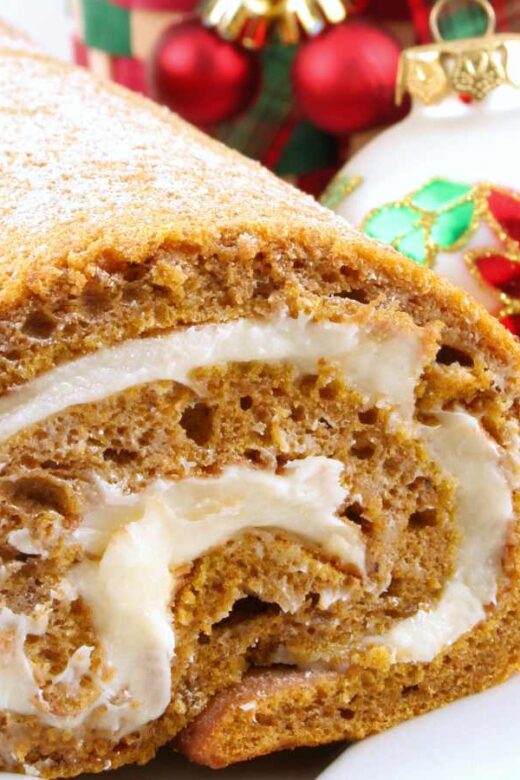 pumpkin roll with cream cheese on a white platter with holiday ornaments in background