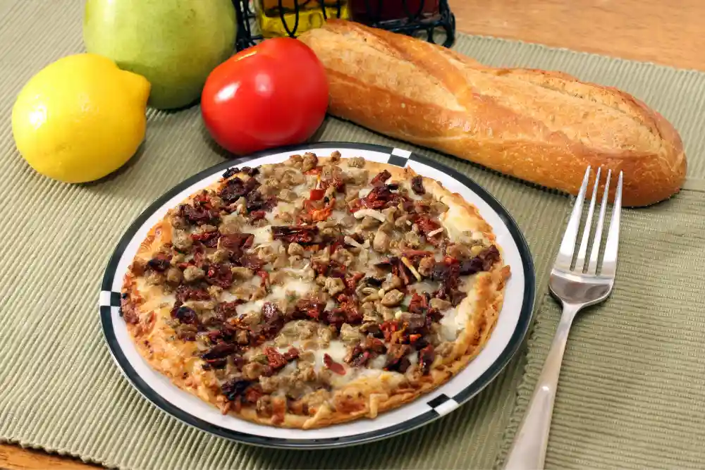 sausage pizza on plate with french bread and vegetable on table