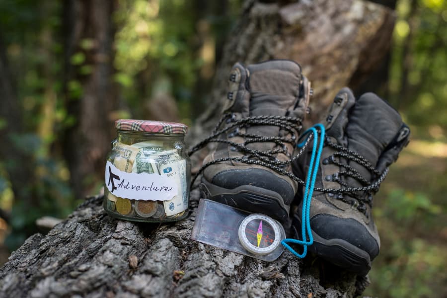 vacation fund jar on treee with hiking boots and compass