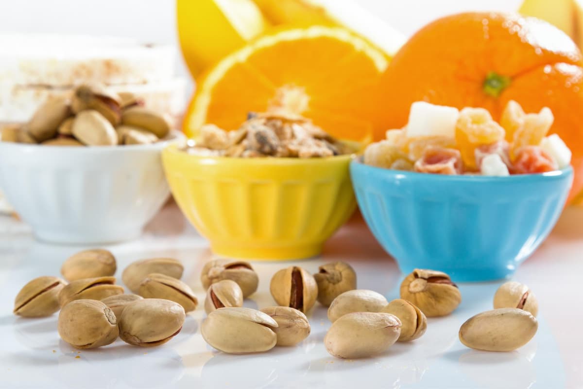Travel snack ideas for kids and adults showing fruits and nuts in brightly colored bowls and oranges in the background