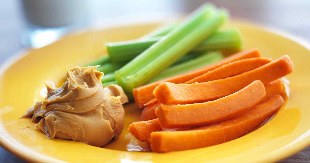 carrots and celery on a yellow plate with a dab of peanut butter