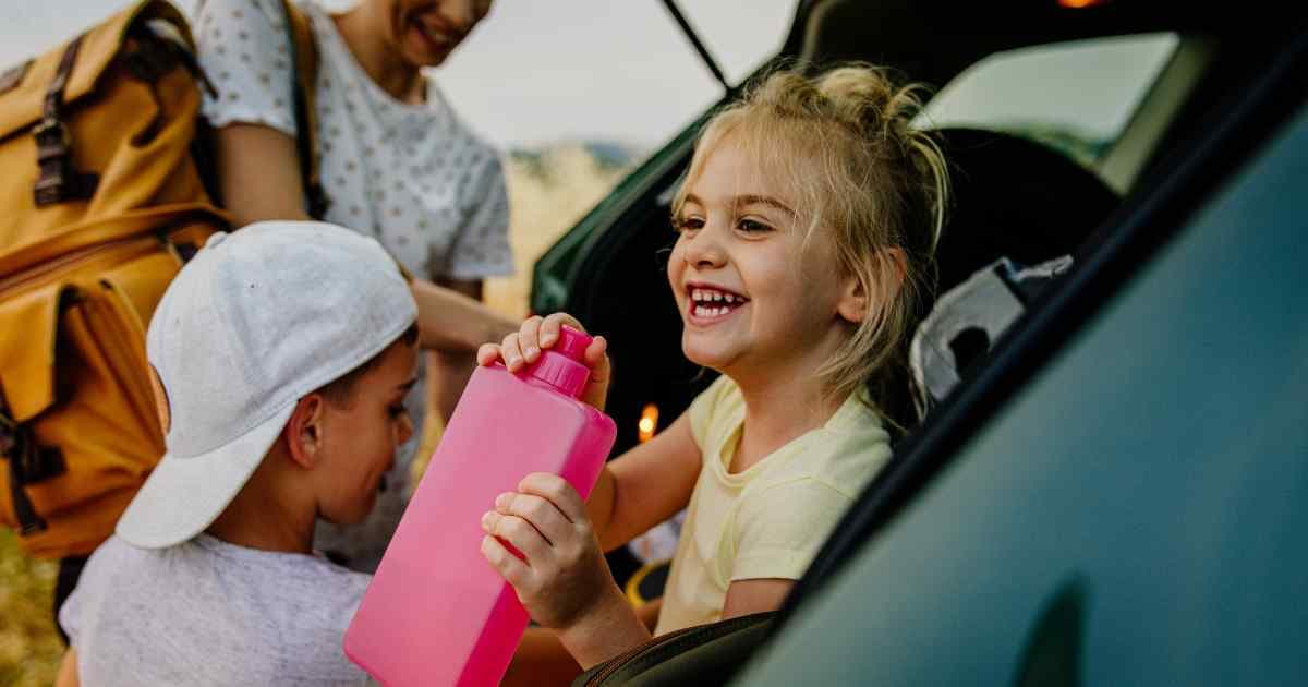girl in car holding pink water bottle while her mom gets a healthy travel snack for little brother
