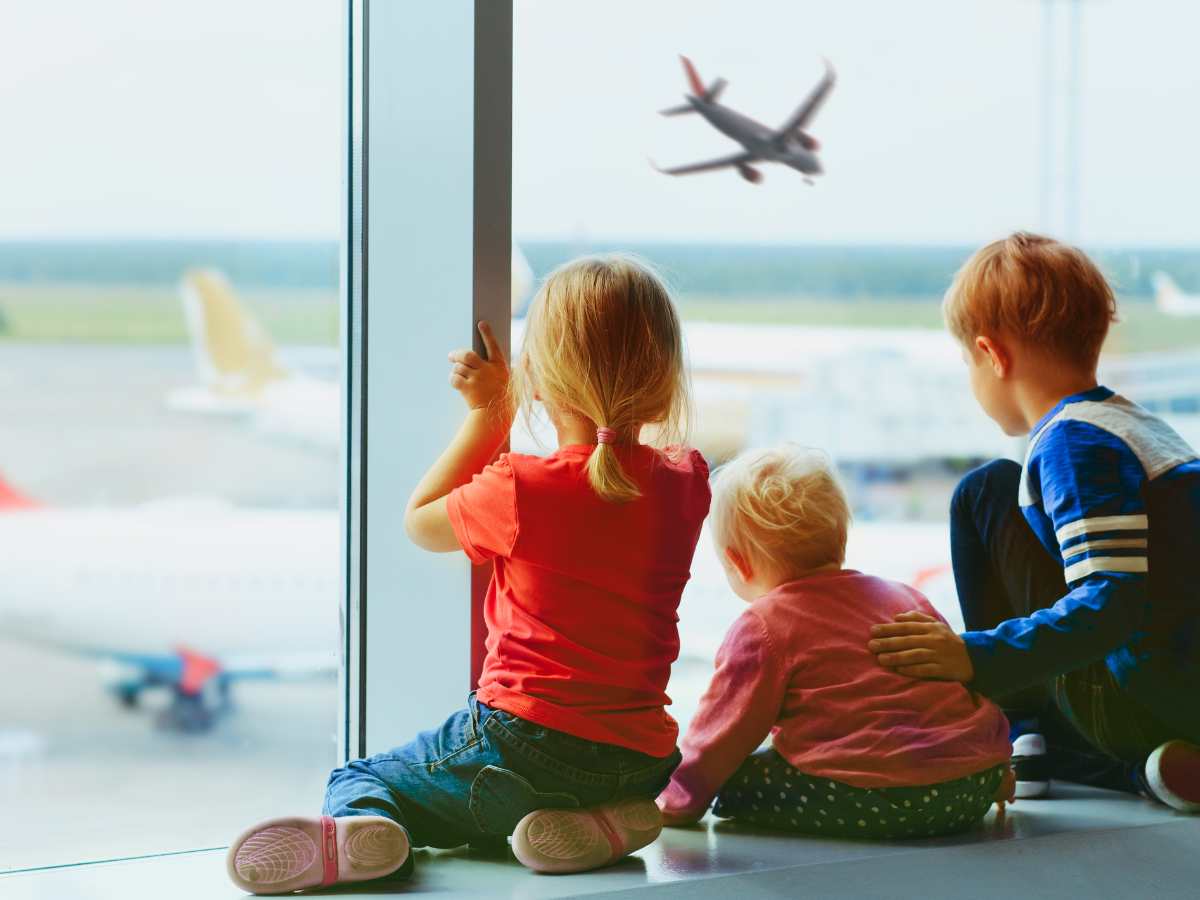 siblings looking out window of airport watching airplanes taking off and landing