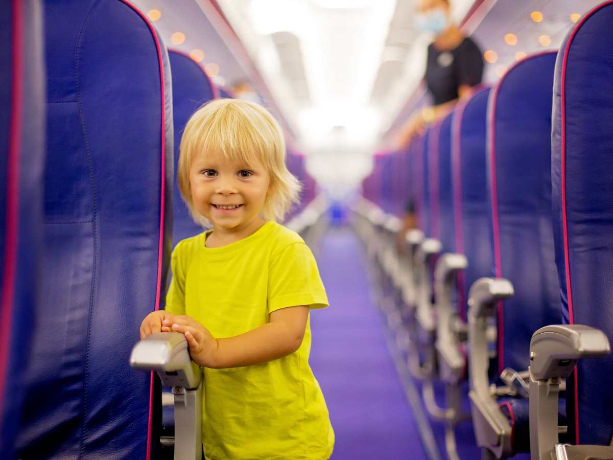 toddler in yellow shirt standing in aisle of airplane