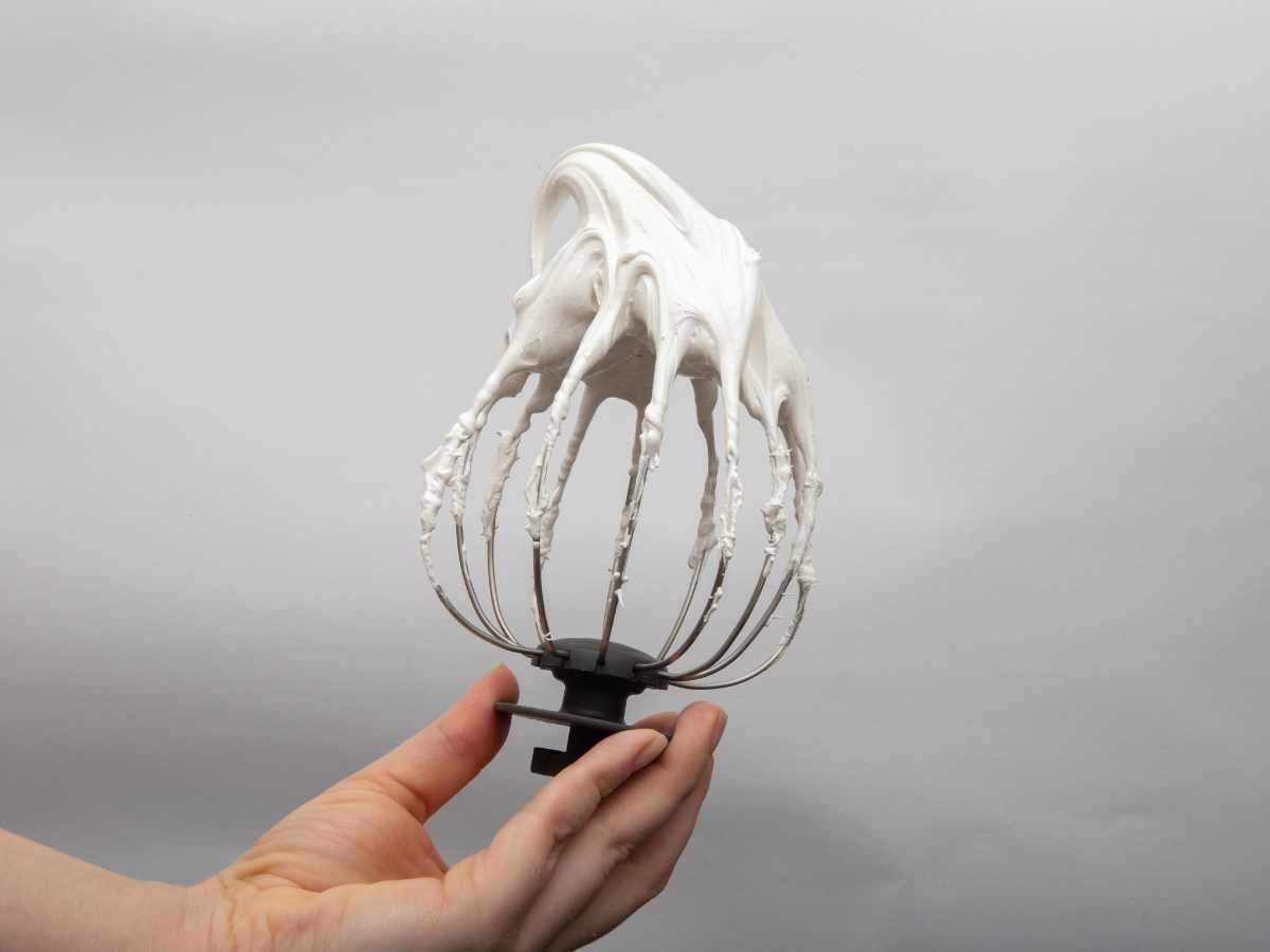 person's hand holding beater from mixer showing stiff peaks making homemade whipped cream