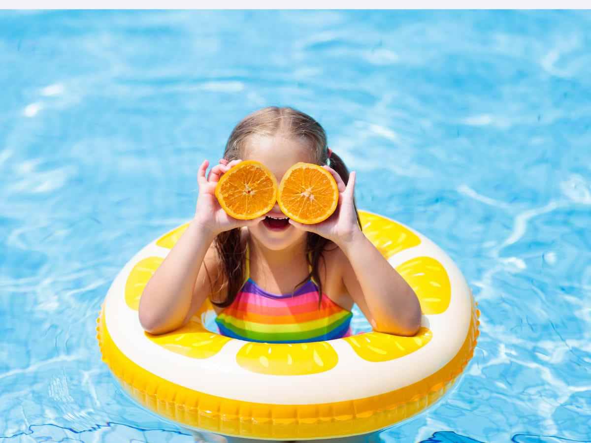 Girl in pool in lemon innertube holding orange slices over her eyes