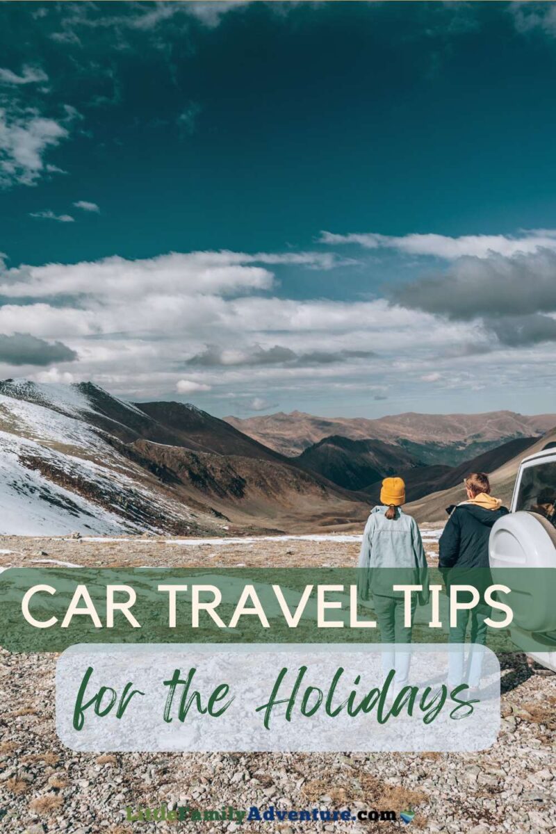 couple standing next to car with snowy windswept landscape on holiday road trip