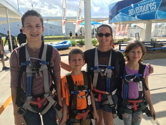 Family in climbing harnesses at Riversport Adventure OKC - Family Fun in Oklahoma City - Zip down 72 foot slides, climb the adventure ropes course, zip line across the Oklahoma river, or don the whitewater rapids in a raft for a family adventure you won't soon forget