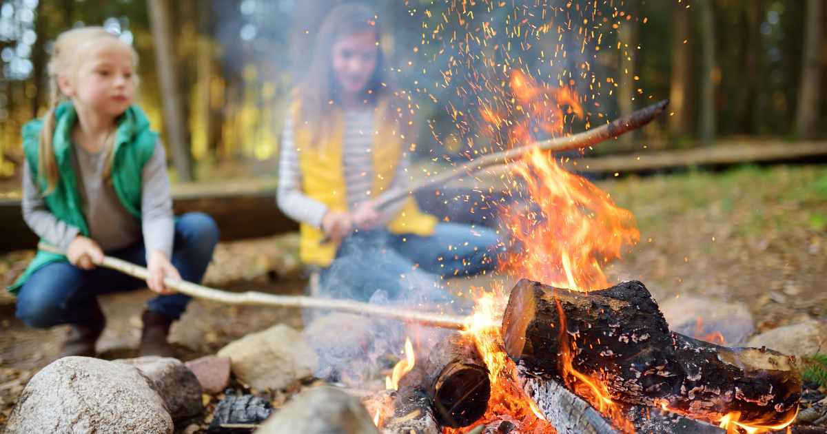 two girls poking sticks in a campfire wearing flannels