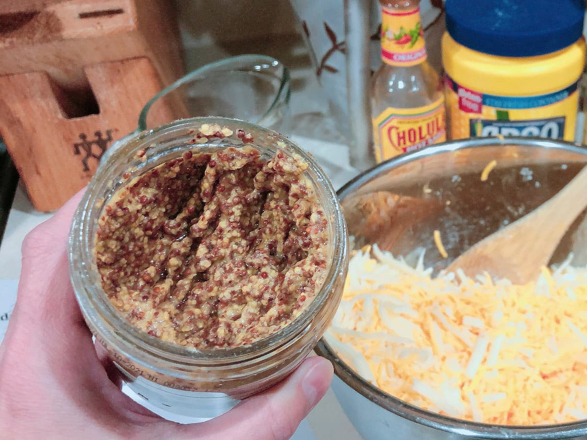 whole grain mustard in jar next to shreadded cheese bowl