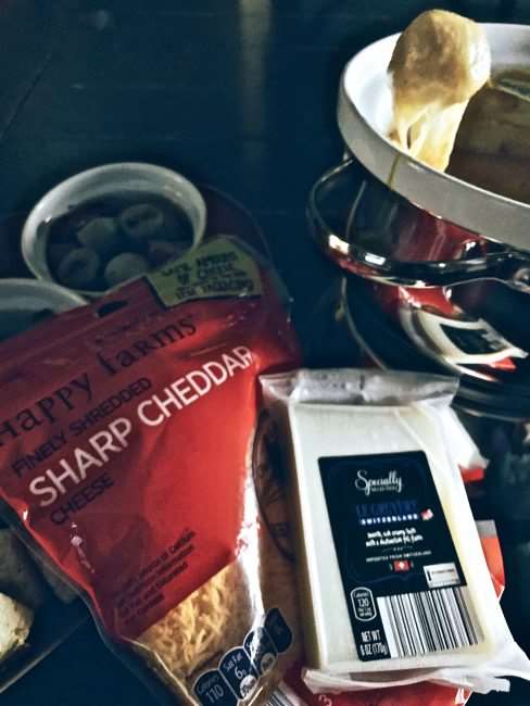 bread dipped in cheese fondue with the packaging of the two types of cheese used shown