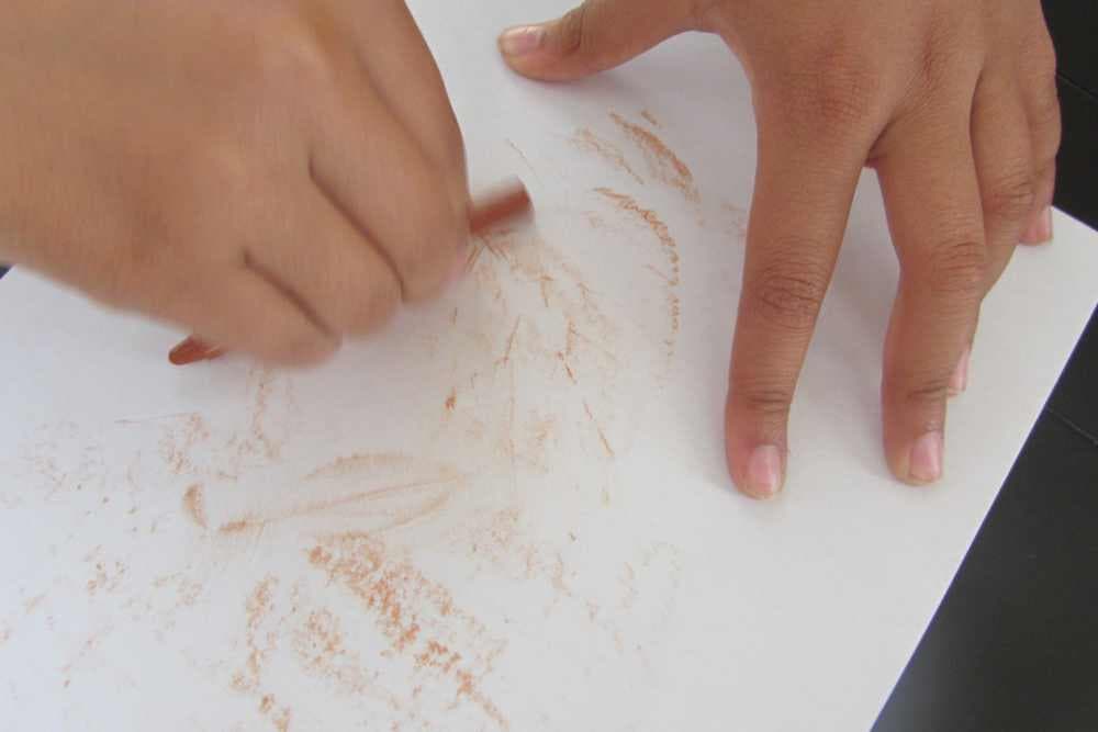 girl holding brown crayon horizontally to make leaf rubbings