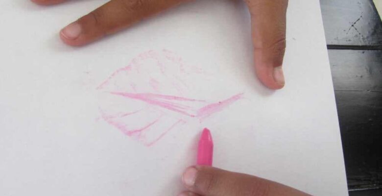 girl holding pink crayon to make nature leaf rubbing on white paper