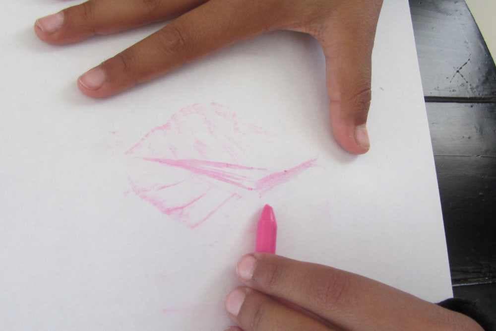 girl holding pink crayon to make nature leaf rubbing on white paper