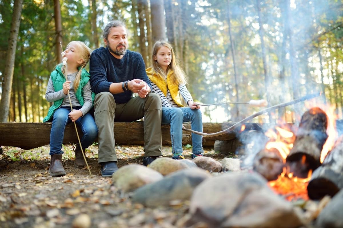 father and daughters roasting marshmallows over fire