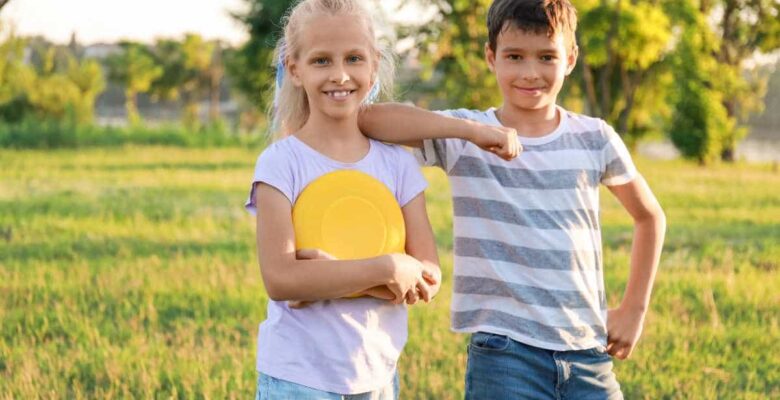 sister and brother holding yellow frisbee in grassy field