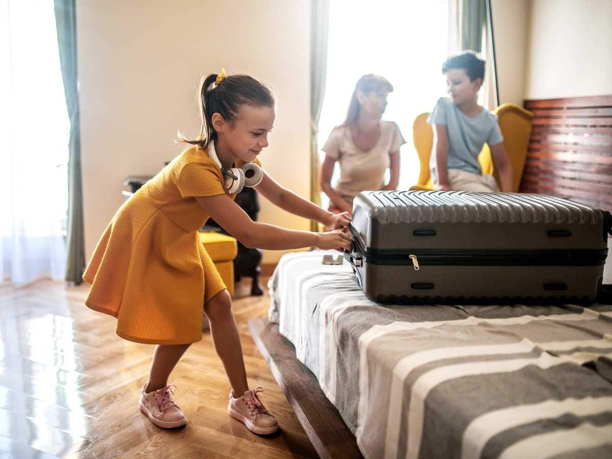 Girl closing suitcase and getting settled in htoel room with mom and brother