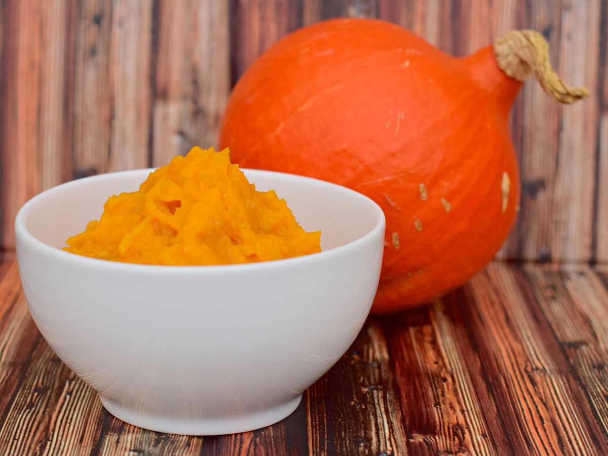 white bowl of pumpkin puree with orange pumpkin in background