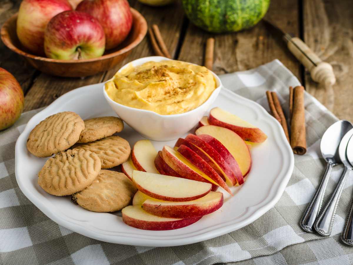 white platter with crisp biscuits, red apple slices, and a bowl of pumpkin pie dip