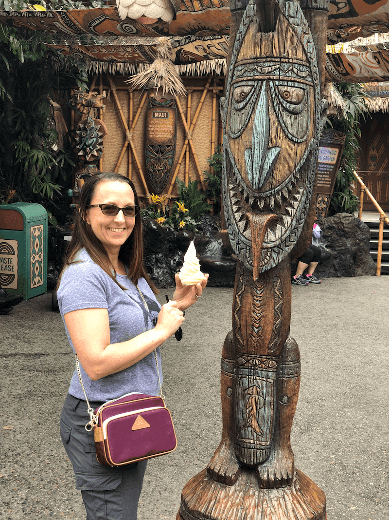 Woman holding Pineapple soft serve in a cup (Dole Whip) in front of a Tiki Statute