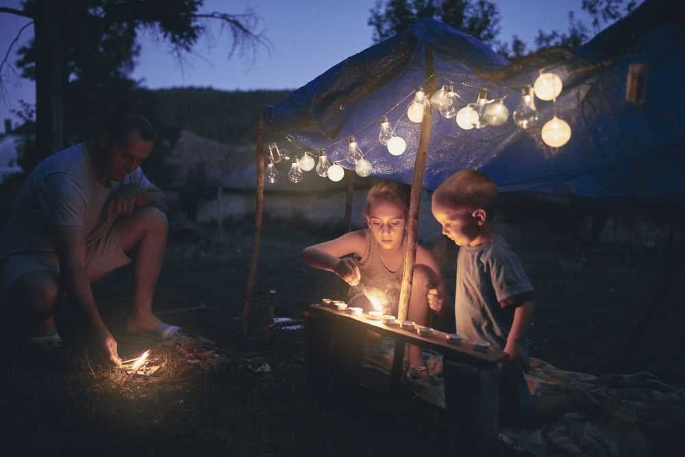 dad with two small kids lighting a campfire and string lights in backyard