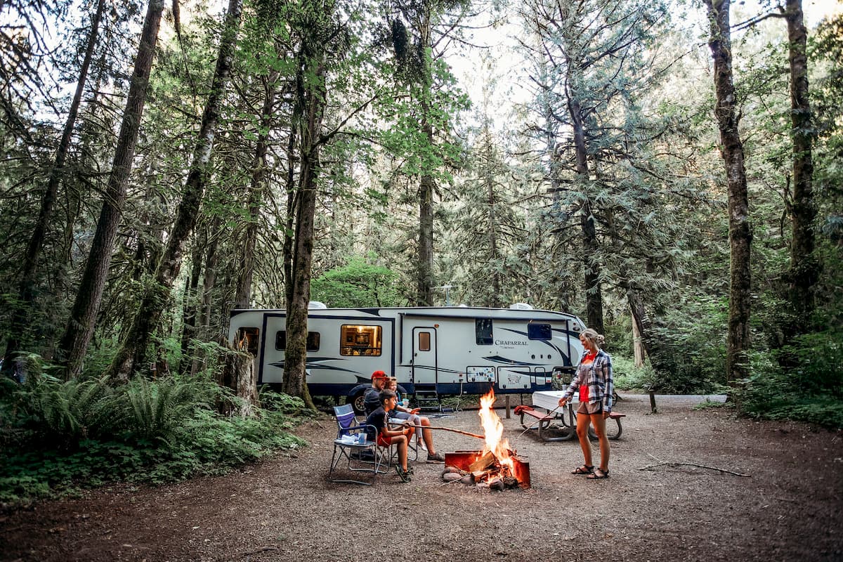 family outside RV around a campfire in woods