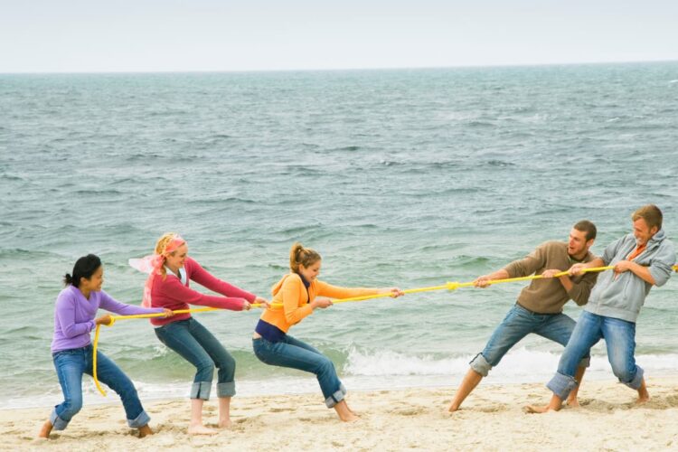 teens playing tug o war on beach