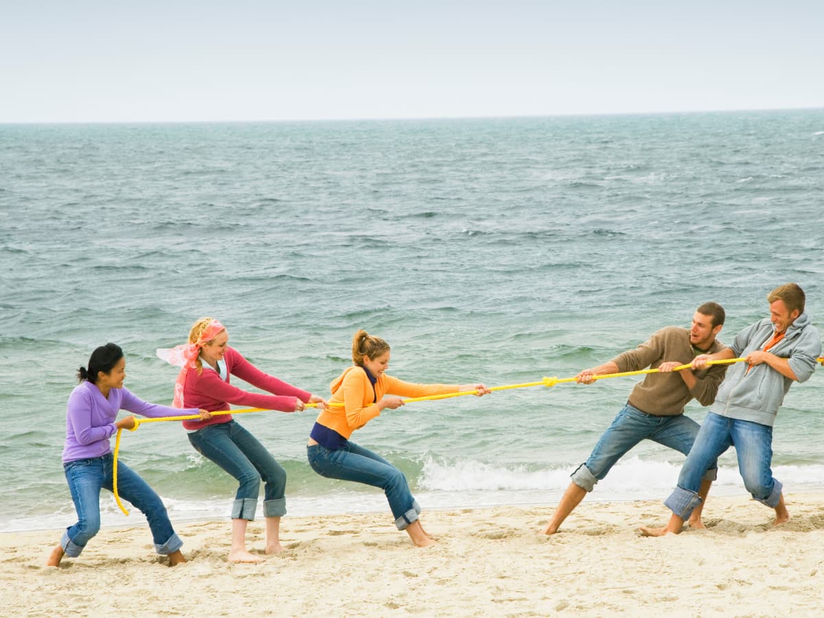 teens playing tug o war on beach