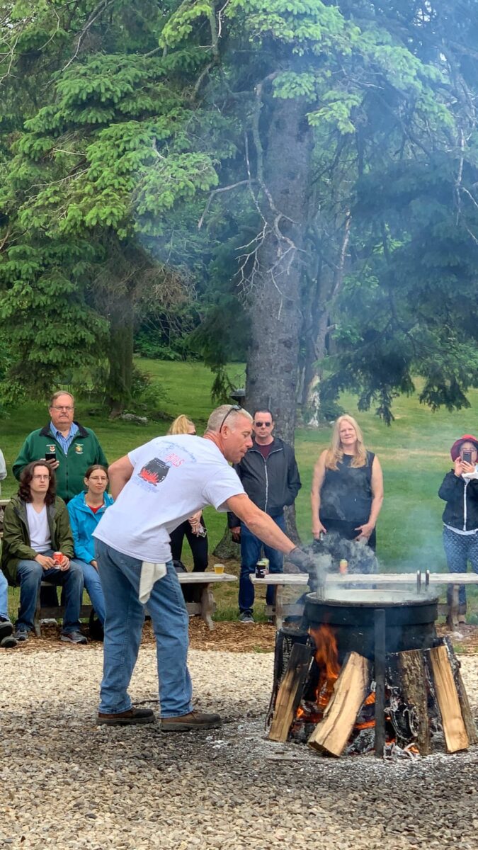 master checking cooking pot over outdoor fire