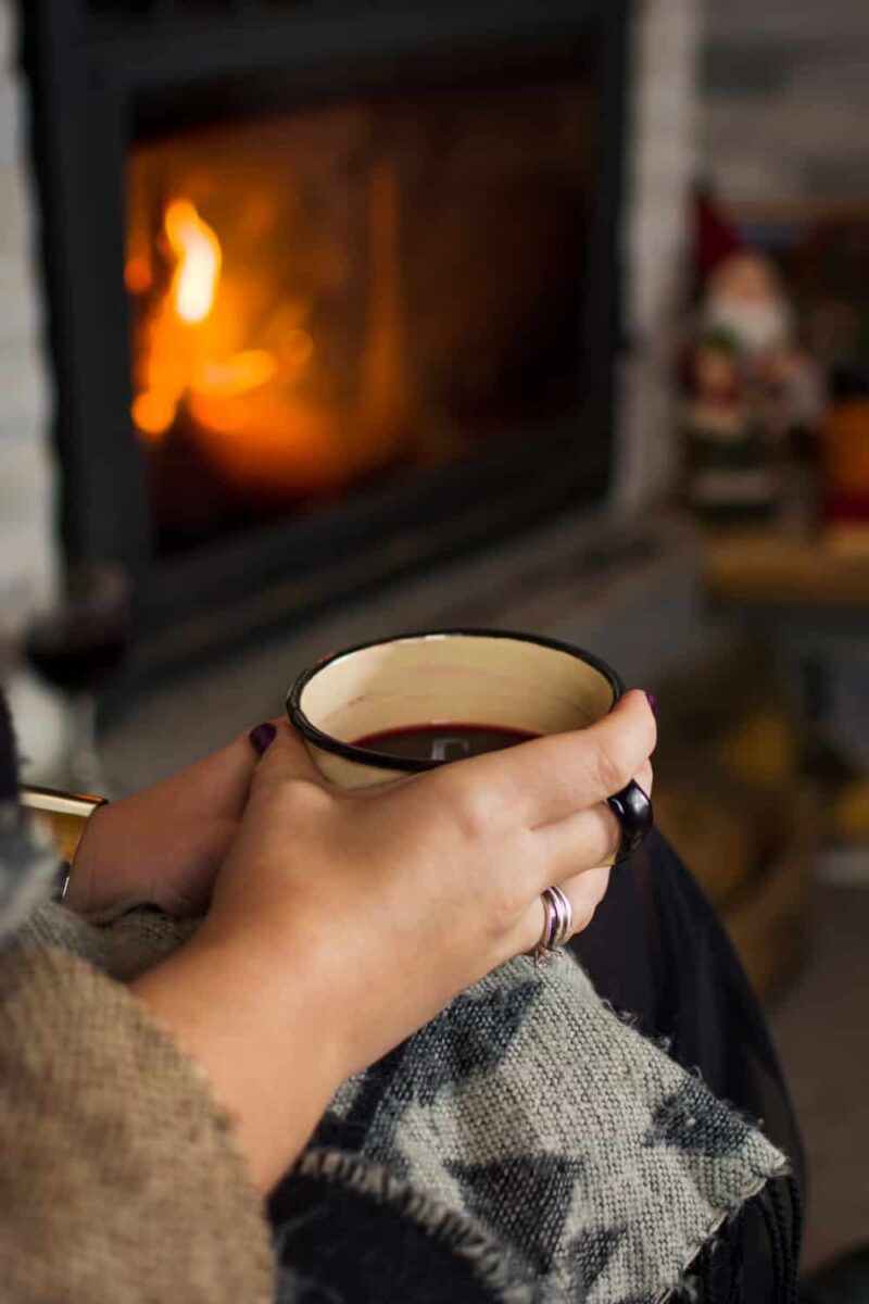 female holding mulled wine cup in front of fire