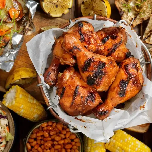 bbq chicken in paper lined basket, grilled bread, corn on cob coleslawm potatoes, an baked beans