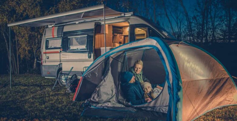 man woman and kid in tent at night with RV in background