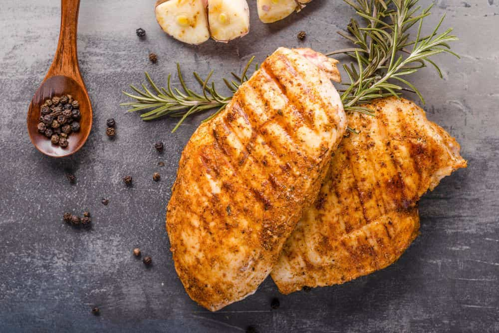 grilled chicken breasts on cytting board with spoonfil of peppercorns