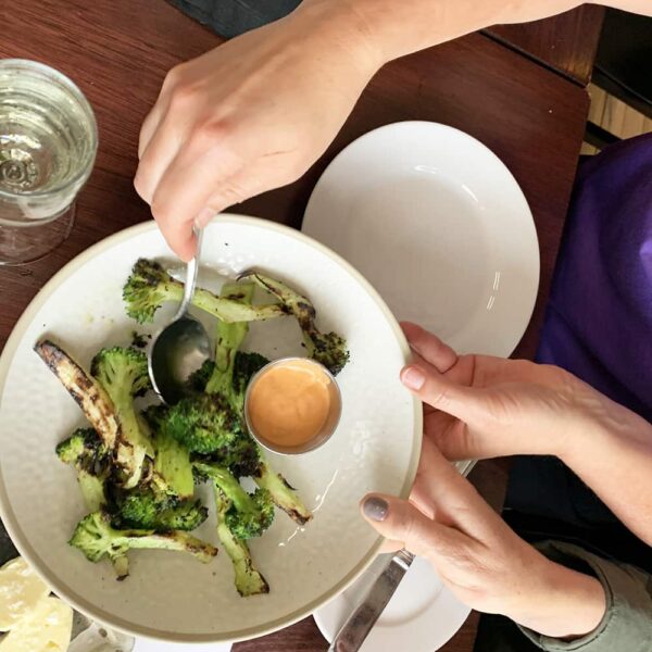 grilled broccoli with dressing on a white plate being served at the Paddock club
