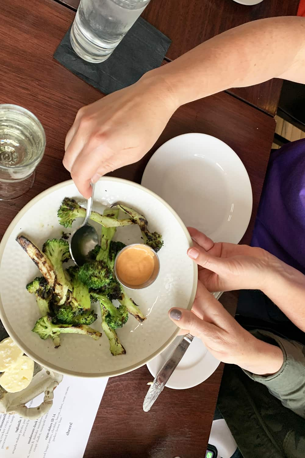 grilled broccoli with dressing on a white plate being served at the Paddock club