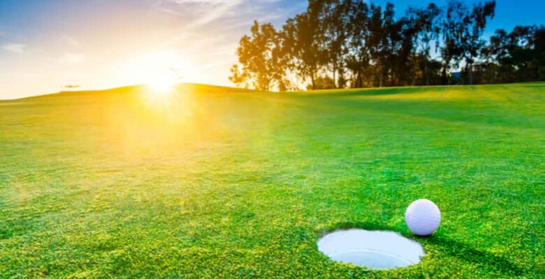golf ball next to hole at sunrise
