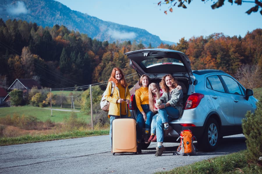 family sitting in back of car for road trip in fall