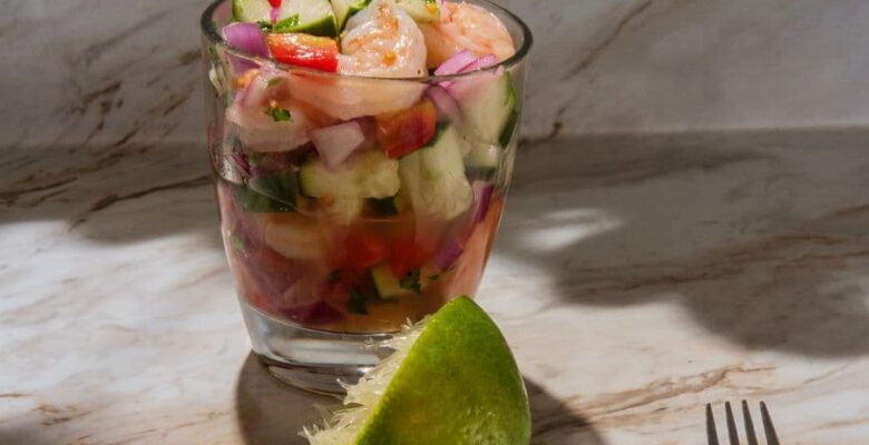 glass of shrimp ceviche with juiced lime in the foreground