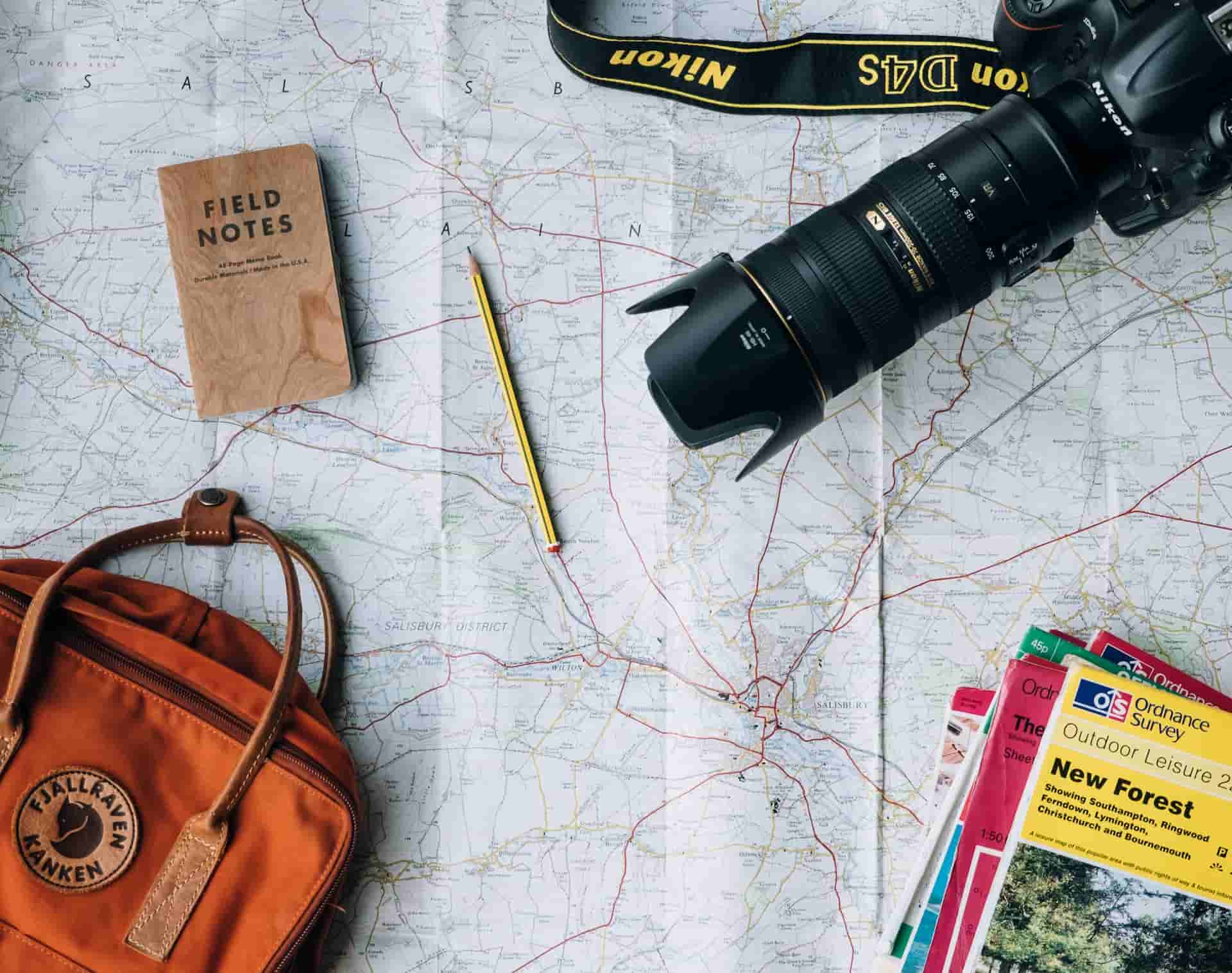 map with travel items like bag, passport, binoculars and books