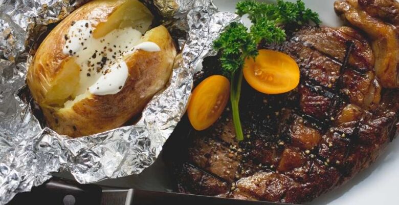 baked potato in foil served with steak and tomatoes on a platter
