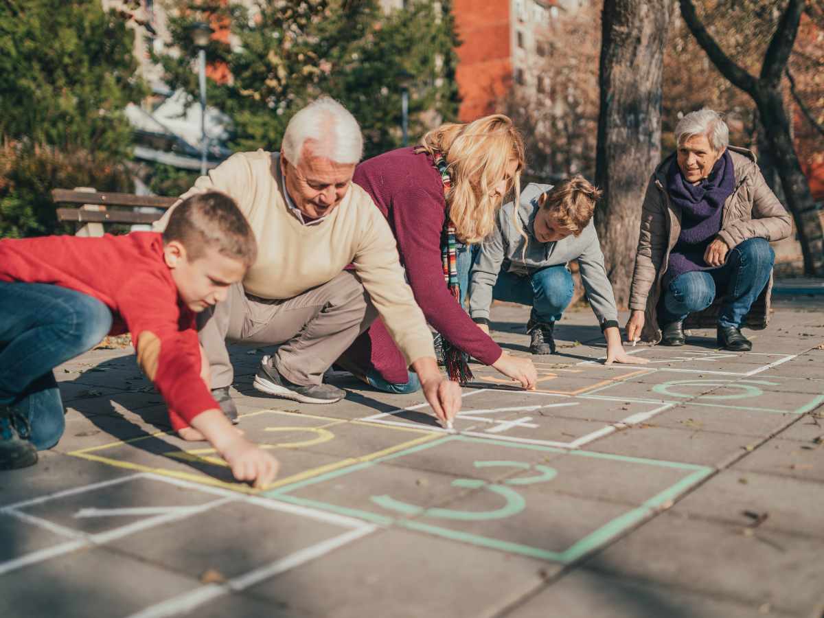 grandparents, parents, and kids drawing hopscotch squares on sidewalk