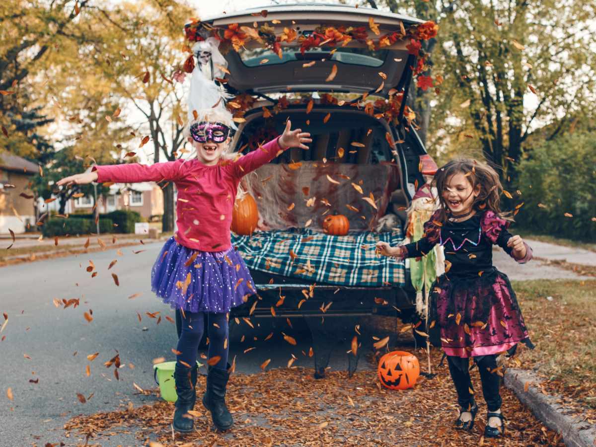 fall family activities with siblings jumping in leaves and throwing them in the air by family car