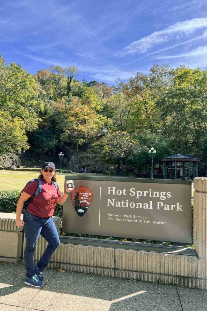 woman with coffee in hand by sign of hot springs national park, arkansas